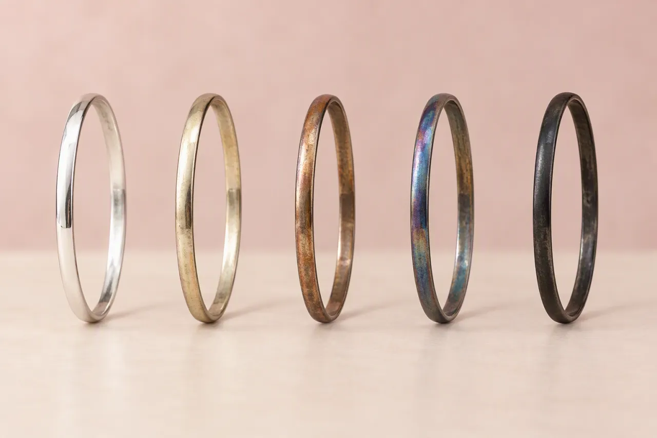 Five plain silver bangles in a row, from bright silver through golden, brown and blue tones to black.