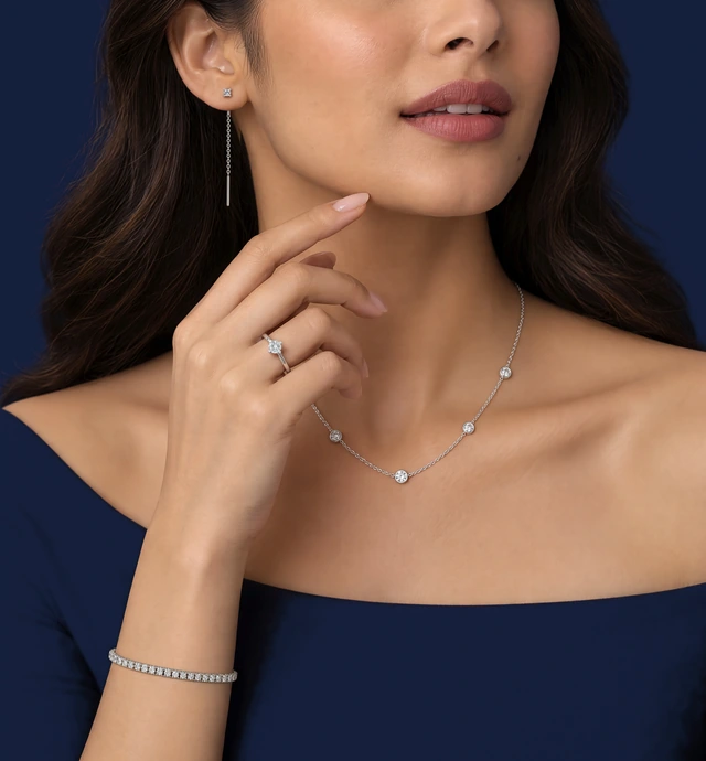 A woman in a navy off-shoulder top, her fingertips at her jaw, wearing the Petite Round Sui Dhaga Earrings, the Classic Solitaire Ring, the Classic Station Necklace and the Classic Tennis Bracelet
