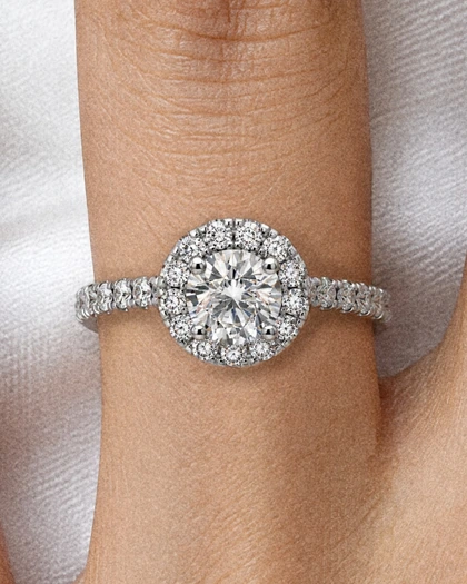 A hand on white silk wearing the Celeste Halo Ring