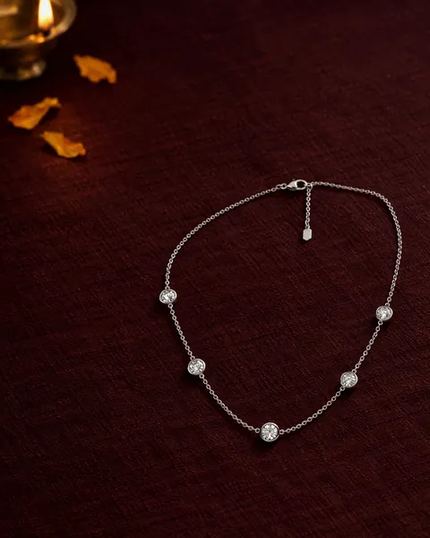 The Classic Station Necklace on dark cloth beside a brass lamp