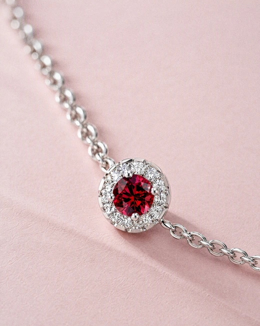 The Celeste Halo Bracelet with a red stone, close on blush paper