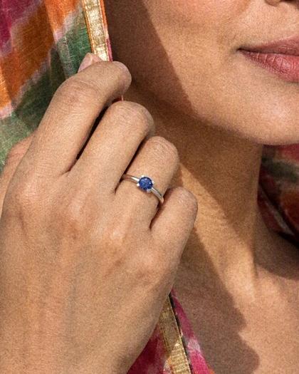 A woman's hand at her jaw, the edge of a pink and green dupatta under her fingers, wearing the Classic Solitaire Ring with a blue stone