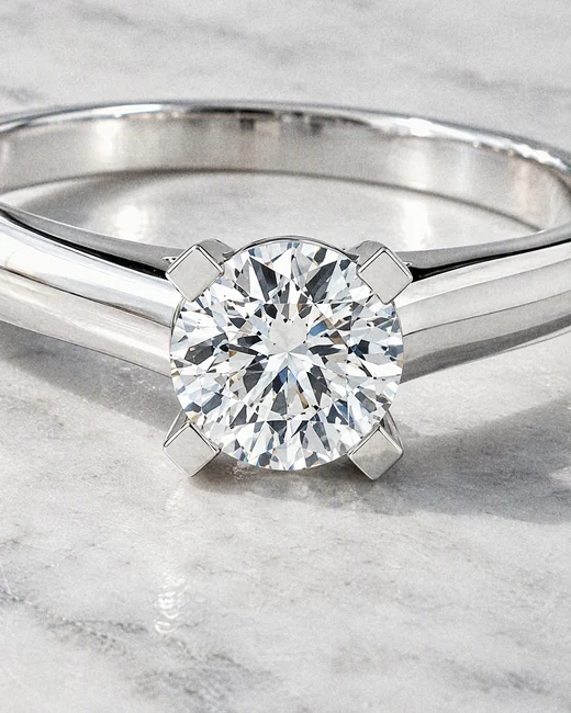 A woman resting her chin on her hand, the Classic Solitaire Ring on her finger