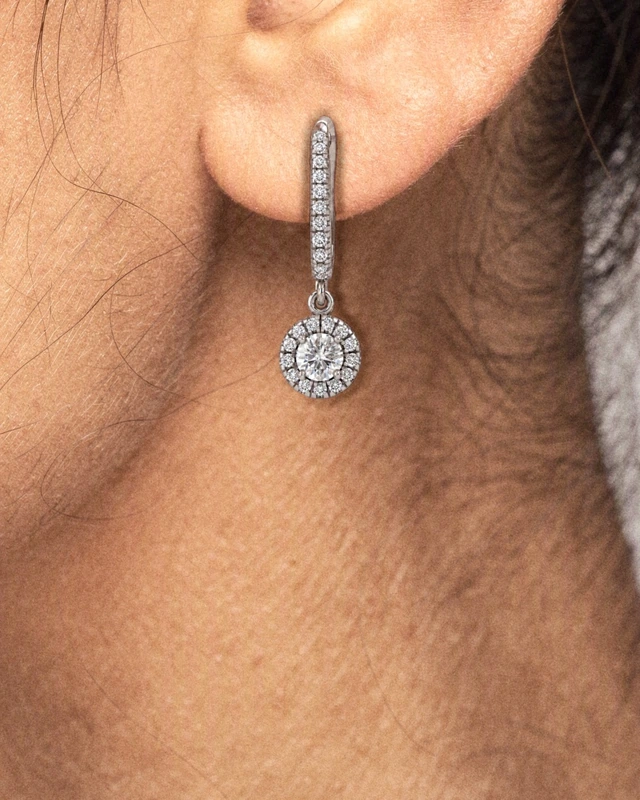 A close view of an ear wearing the Celeste Drop Earrings, the halo drop hanging below the lobe