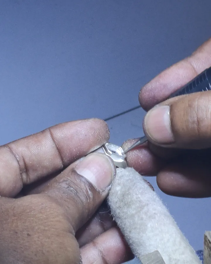A setter’s hands holding a ring against a wooden peg while a stone is set