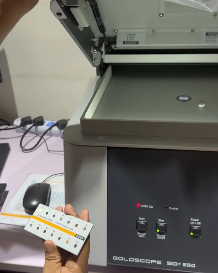 An X-ray fluorescence machine with its lid open and a card of reference standards held beside it